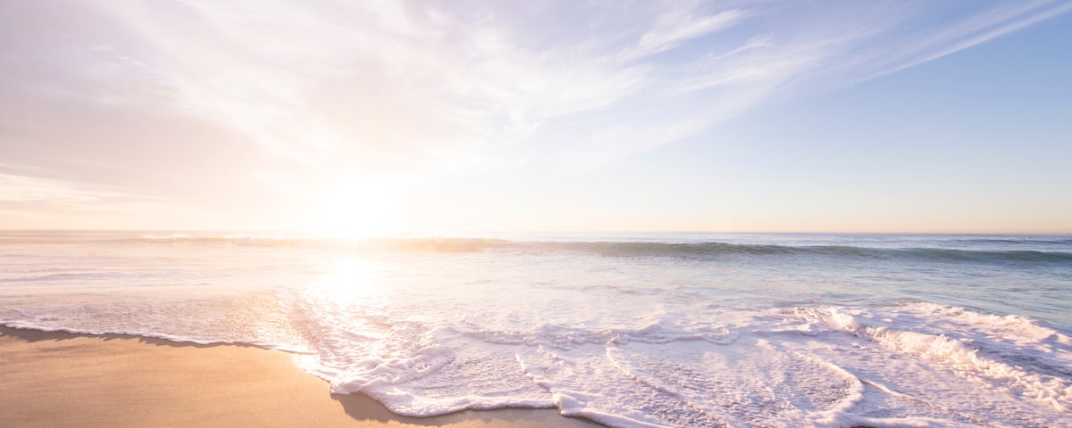 A golden sunrise over a calm shoreline with soft waves at dawn