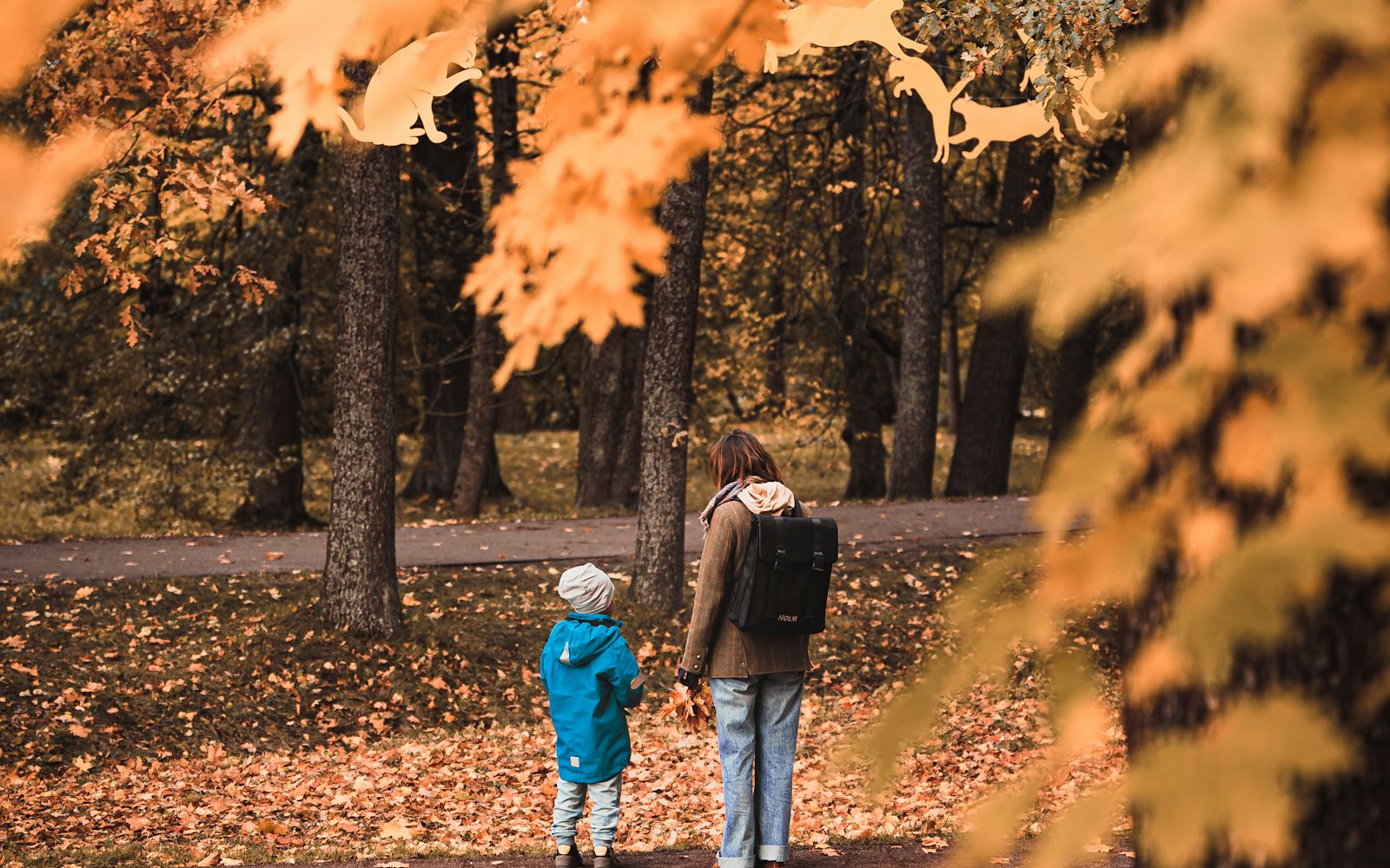 A parent and child walking together under golden autumn leaves