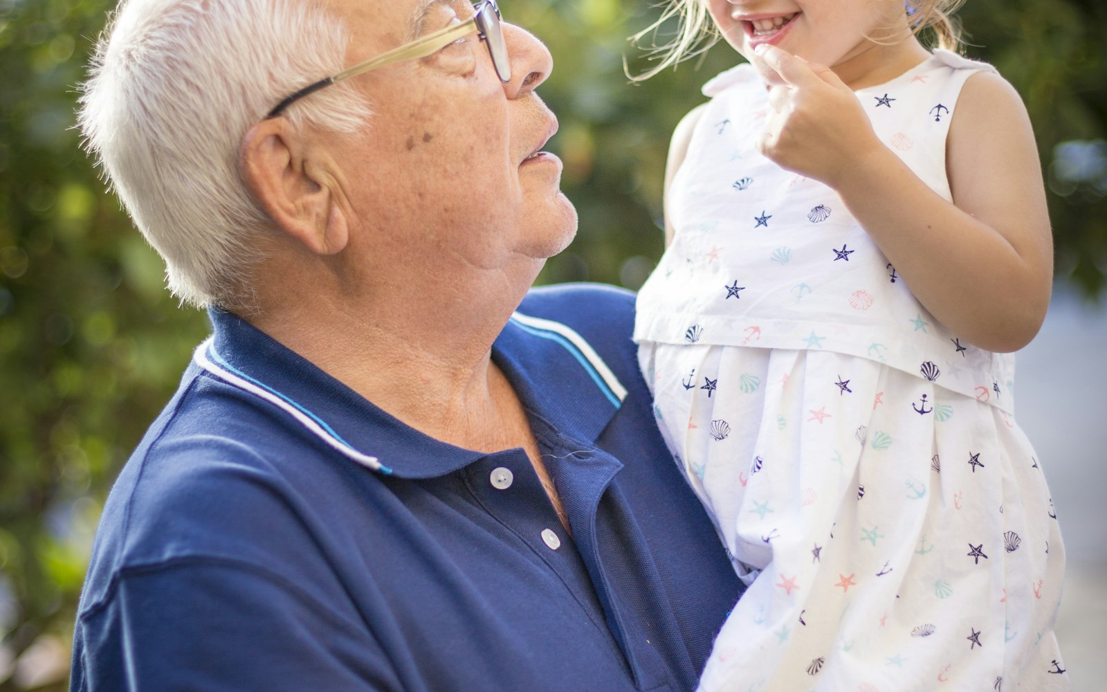 A grandfather smiling as he carries his granddaughter outdoors